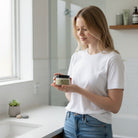 Creamy Don Tolman Divine Body Butter jar with a white lid and label, showcasing rich, nourishing skincare in a natural setting.