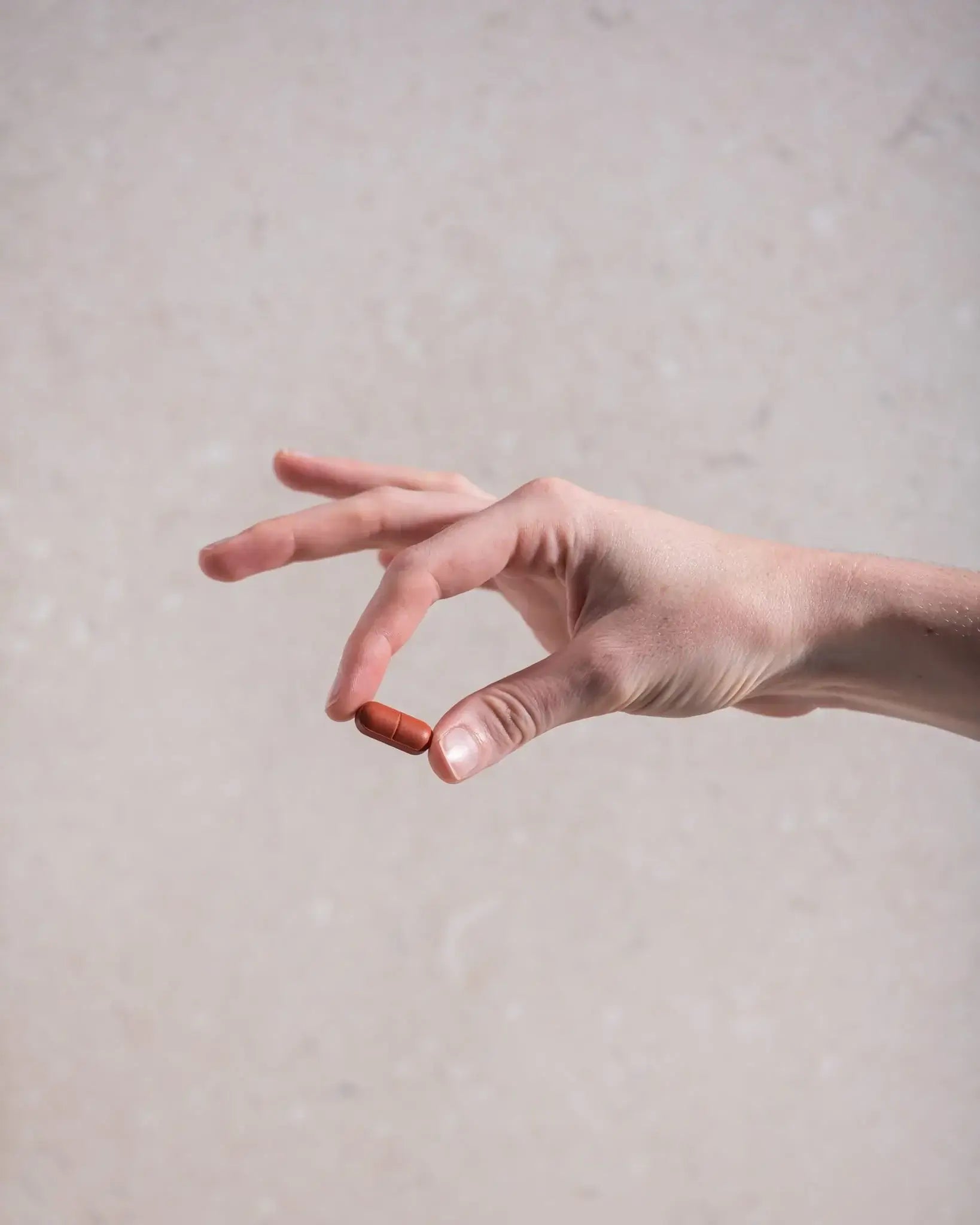 Hand holding a Hawthorn cardiovascular support supplement capsule against a neutral background.